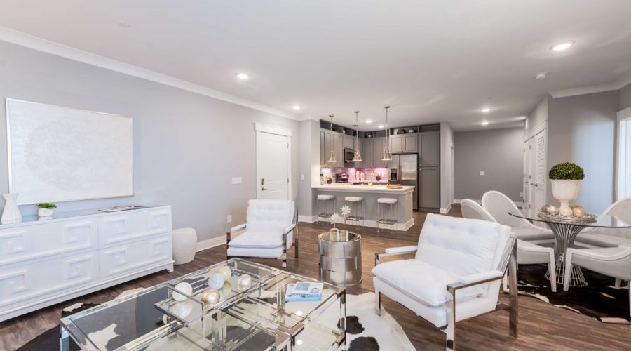 Modern open-concept living room and kitchen with white furniture and stainless steel appliances.