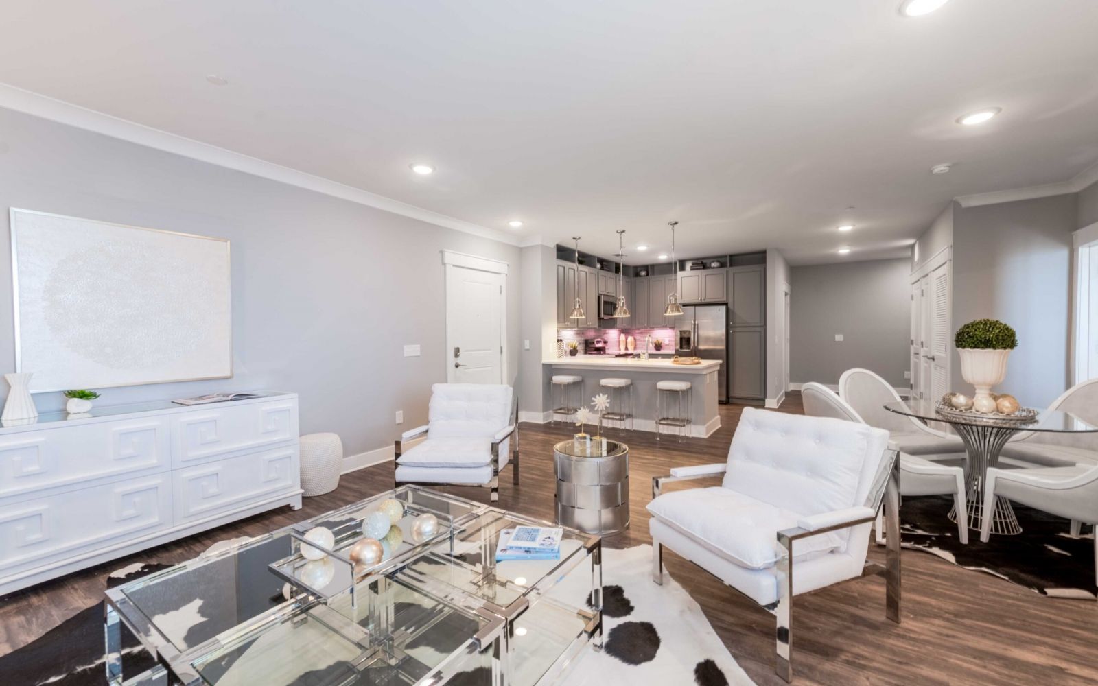 Modern open-concept living room and kitchen with white furniture and stainless steel appliances.