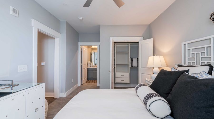 Modern bedroom at Carolina Square with a neat bed, open closet, dresser, and view into a bathroom near UNC Chapel Hill.