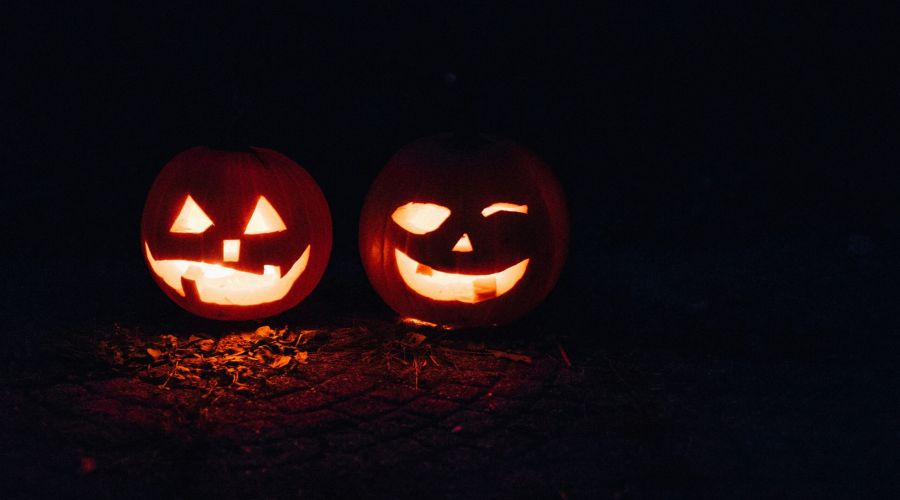 Two glowing jack-o’-lanterns with carved faces sit side by side on the ground in the dark.