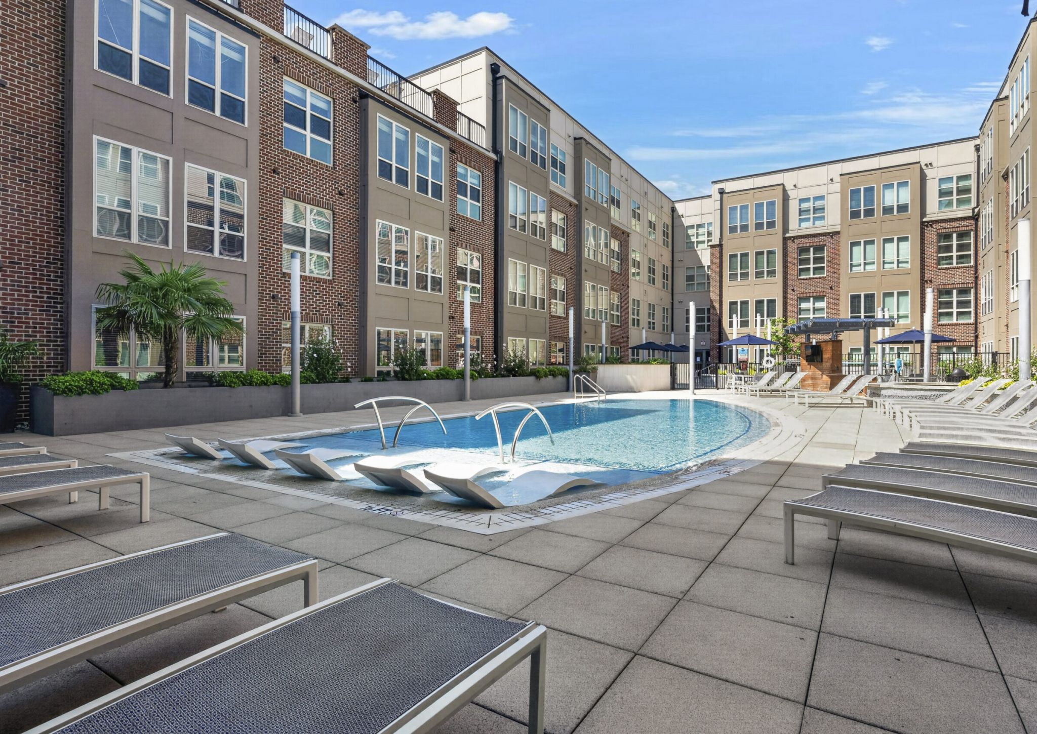 Outdoor pool area with lounge chairs, surrounded by modern apartment buildings under a clear blue sky.