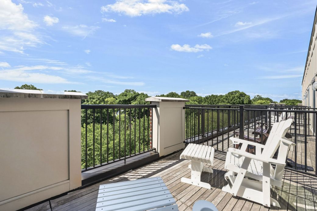 Rooftop deck with wooden chairs and railing overlooking green trees under a blue sky with clouds.
