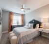 Modern bedroom with a bed, two stools, dresser, lamp, and large window with curtains letting in daylight.