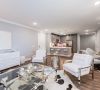 Modern, open-concept living room and kitchen with white and gray décor, glass table, and accent chairs.